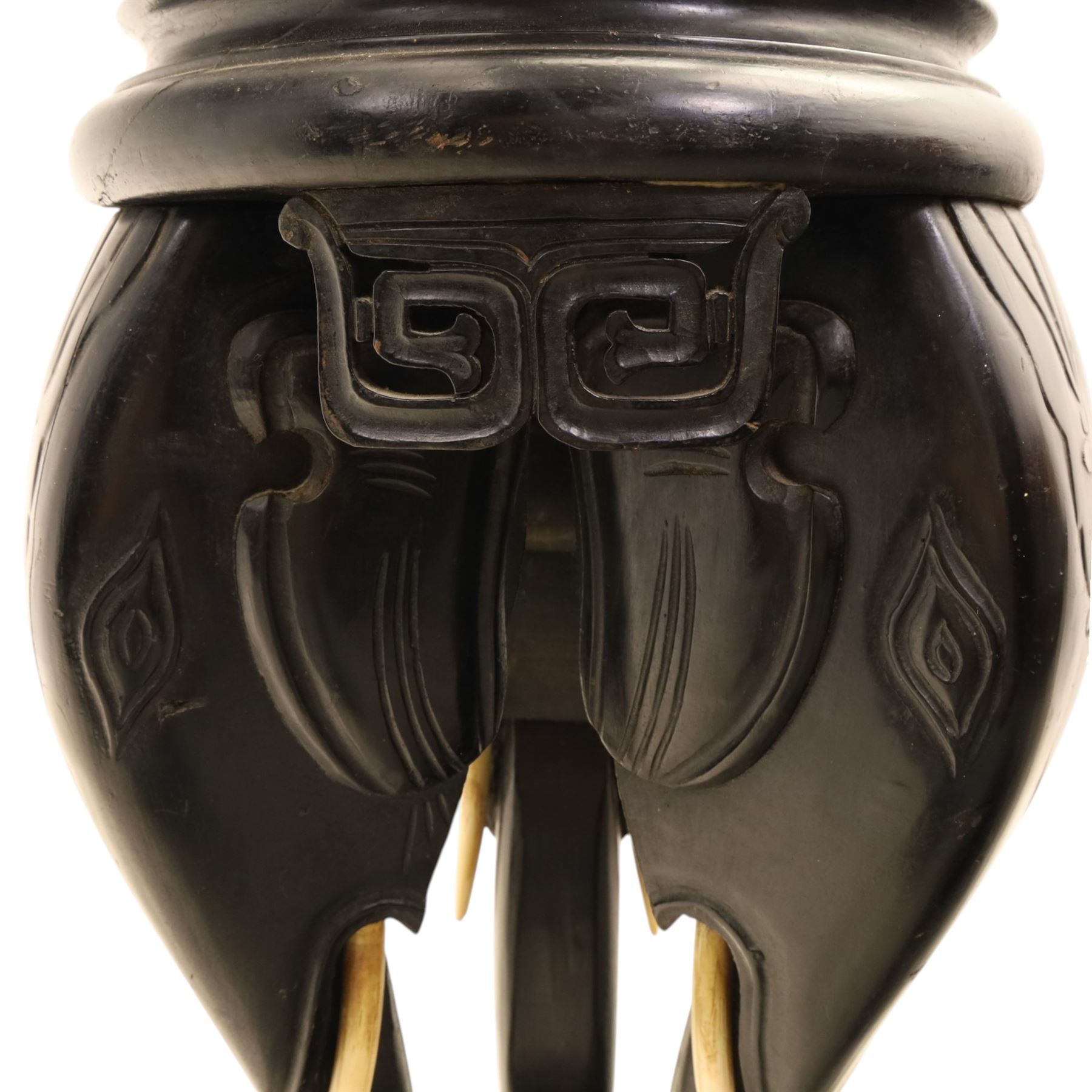 Oriental design black lacquered jardinière stand, circular moulded top with raised rim, the base formed as three elephant heads with carved ears and simulated tusks, on shaped supports with paw terminals