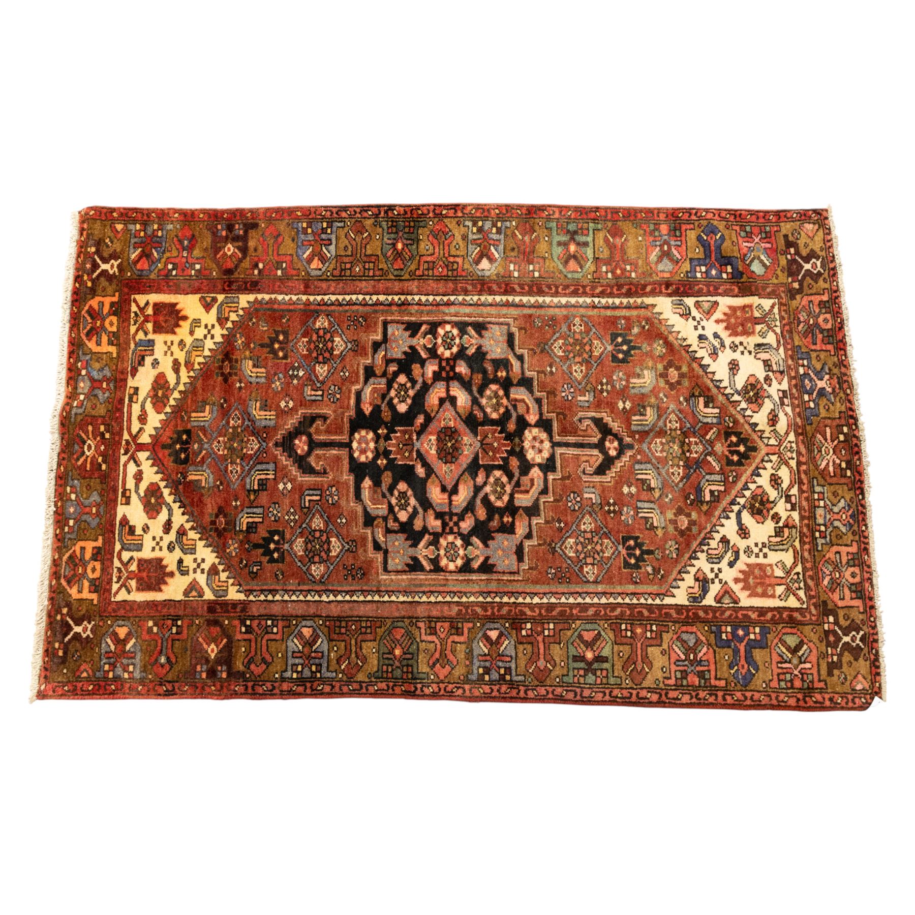 North West Persian Zanjan hand-knotted rug, madder-red field with a central stepped lozenge medallion enclosing stylized geometric floral motifs in indigo, ivory, and brown, angular spandrels filled with tribal devices and framed by a series of geometric borders with latch-hook rosette and leaf motifs, with cotton fringe ends  