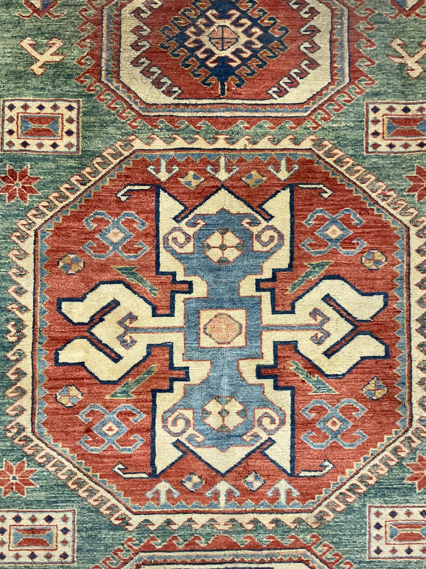 Kazakh rug, pale green ground field with three part medallion, three band border decorated with stylised plant motifs