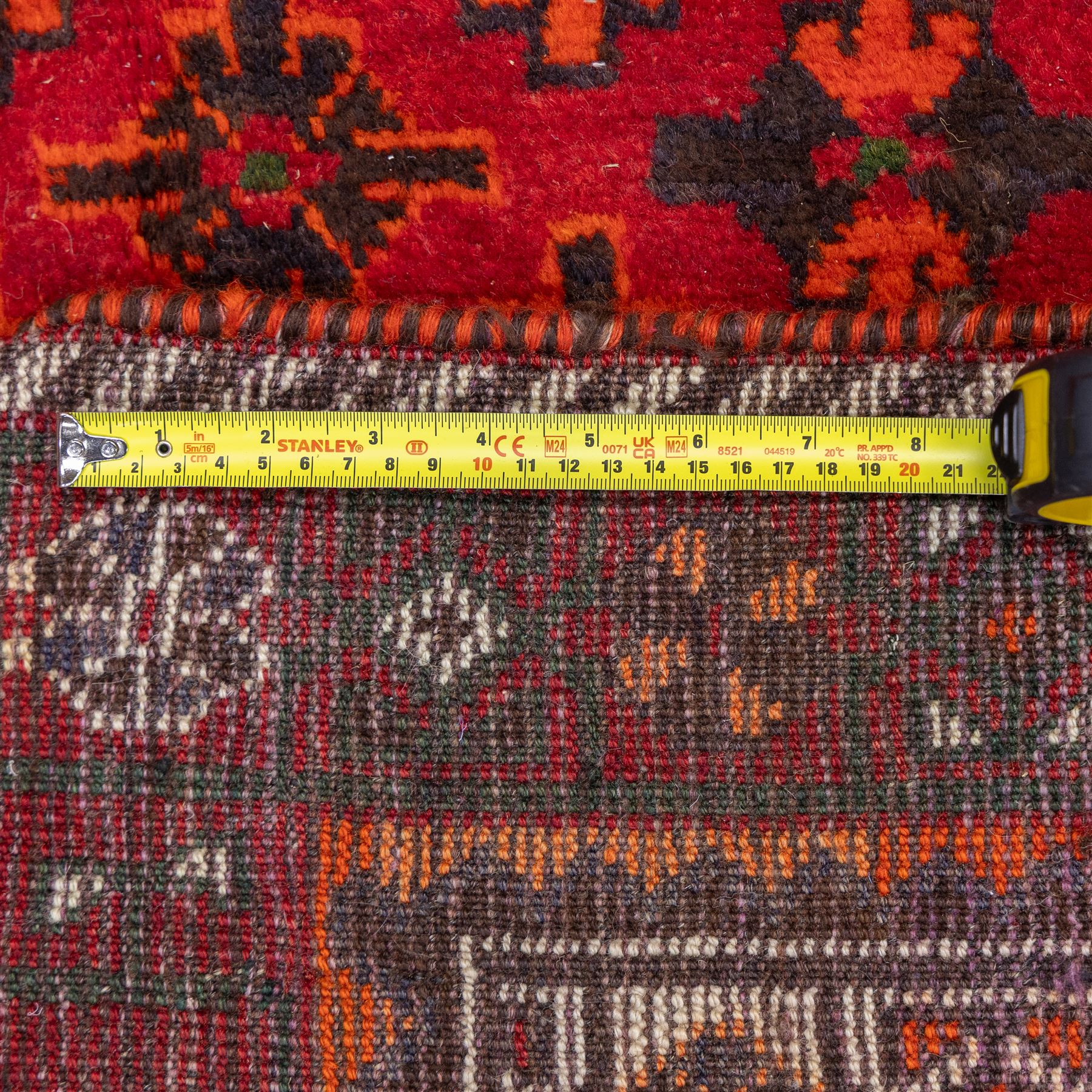 South West Persian Lori hand-knotted rug,  deep crimson field with a stepped lozenge medallion enclosing stylised floral motifs within multiple geometric borders of indigo, ivory, and green, with fringe ends 