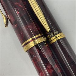 Pelikan Souveran Ruby Red fountain pen, the marbled resin barrel and cap with gilt beak shaped clip and double cap band with gold bi-colour nib stamped 14C-585 M, together with matching ballpoint, Pelikan New Classic fountain pen with marbled maroon barrel and gold nib stamped 14C-585 B, largest L13.5cm (3)
