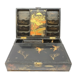  A 20th century Chinese black lacquer and gilt detailed writing box, decorated with figures, pagodas and cranes amidst a mountainous landscape, the hinged cover opening to reveal a compartmented interior and fold out baize lined slope, H20cm L46.5cm D31.5cm.   