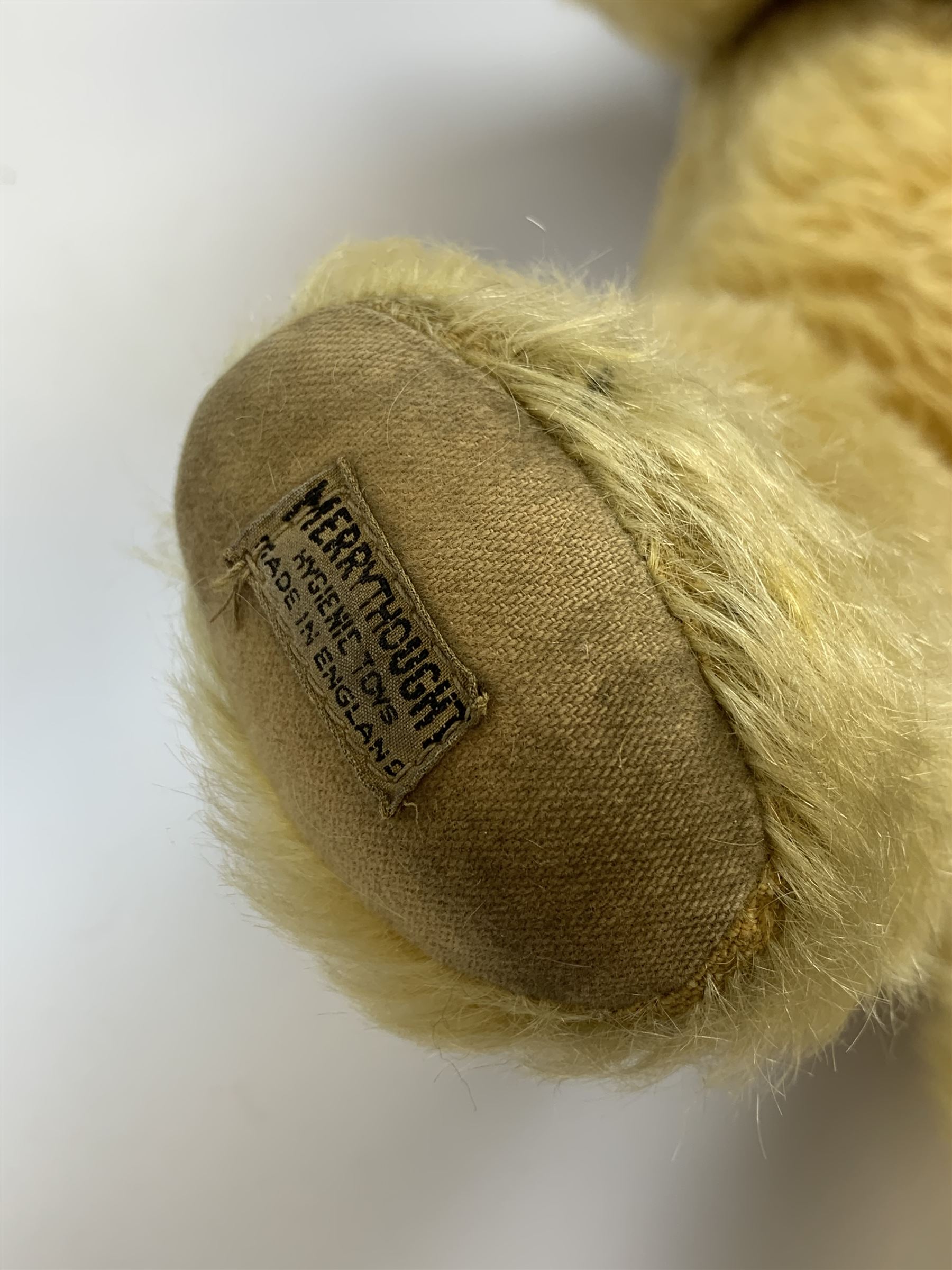 Merrythought Hygienic Toys large 'Magnet' teddy bear c1930s with plush body, swivel jointed head with glass eyes and vertically stitched nose and mouth and jointed limbs,  celluloid wishbone button to right ear and stitched label under right pad H22