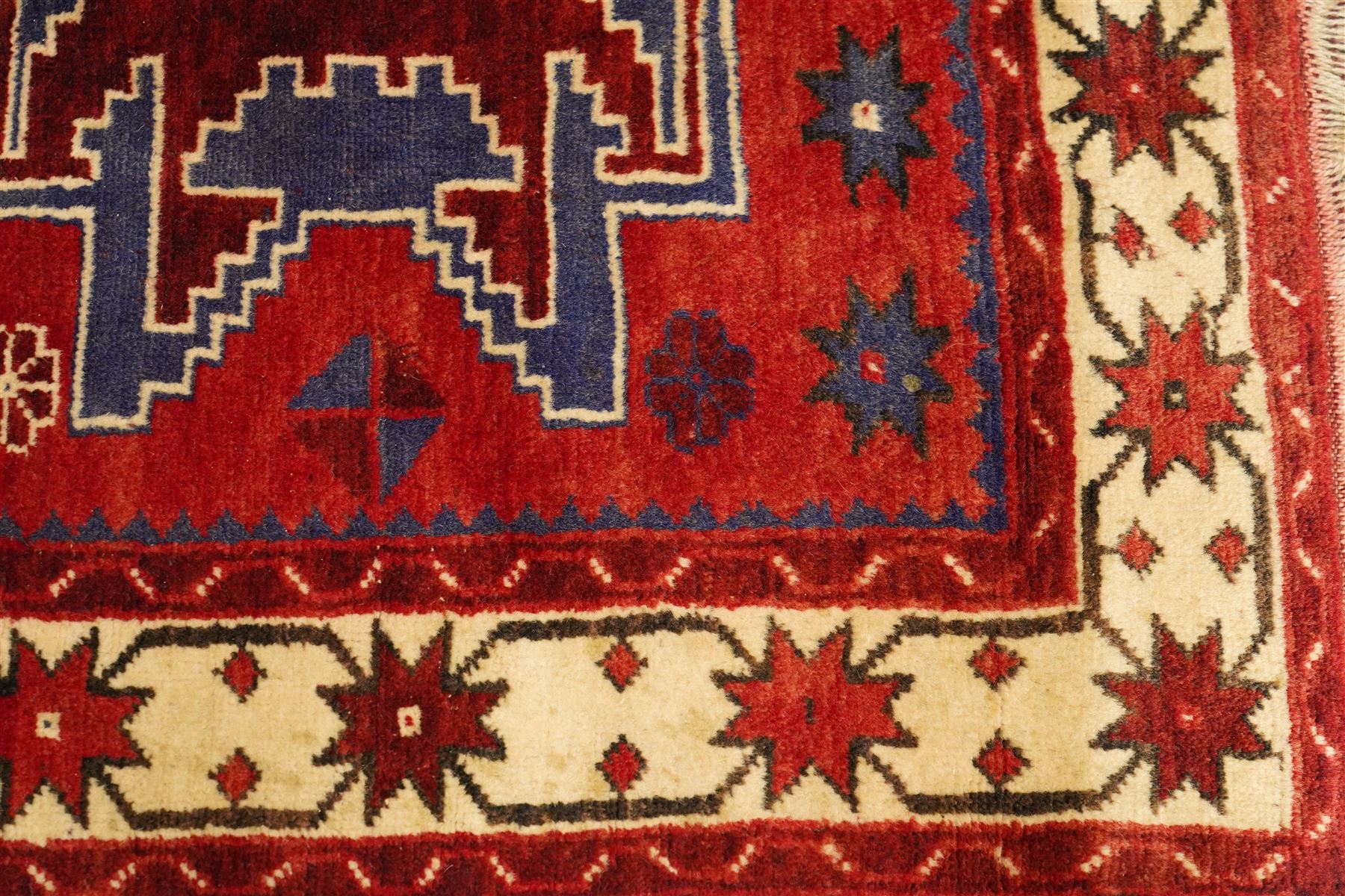 Caucasian Kazak hand-knotted rug, madder red ground with three large stepped geometric medallions in dark blue, ivory and red, surrounded by stylised star and flowerhead motifs, enclosed by ivory border with repeating eight-pointed stars, fringed ends