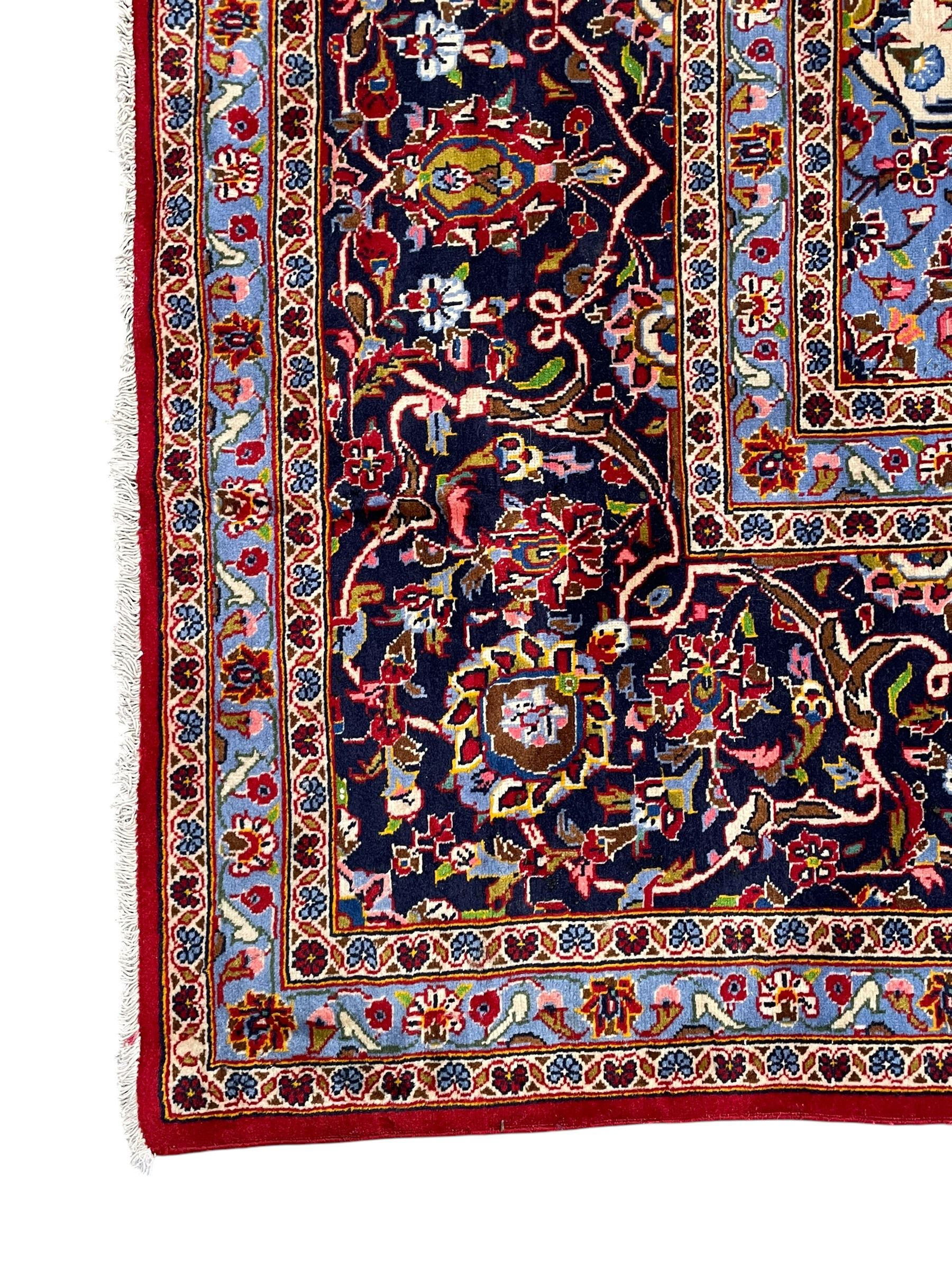 Persian Kashan crimson ground carpet, floral pattern indigo ground central medallion and matching spandrels, the field decorated densely with scrolling foliate patterns and floral motifs, the main border decorated with scrolling branches and palmettes, within floral pattern guard stripes