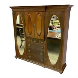 Early 20th century mahogany wardrobe, break front with projecting moulded cornice, the centre fitted with double cupboard over three short and three long drawers, flanked by two full height doors with oval bevelled mirrors, on turned feet