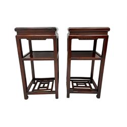 Pair Chinese lacquered hardwood stands, square moulded top above panelled undertier and constructed rail undertier, the frieze carved with scrolls, all united by square supports