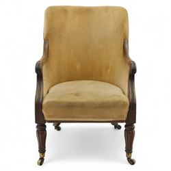 William IV mahogany library armchair, beige velvet upholstered back and padded seat with piping and scroll carved arms, reeded uprights, raised on tapered reeded front legs and out-swept back legs with brass castors 