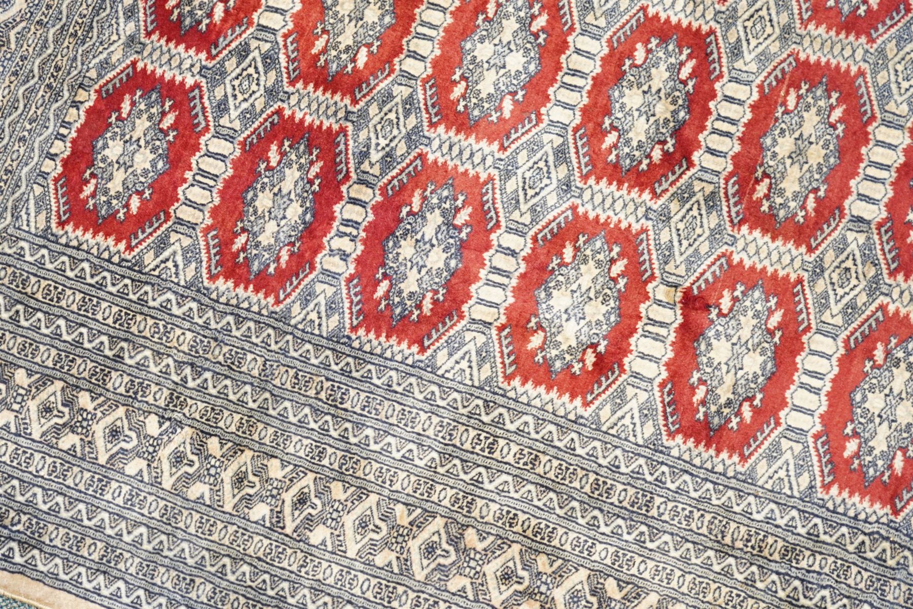 Jaldar Bokhara crimson and pale ground carpet, the field decorated with five rows of Gul motifs, within intricate multi-band border decorated with repeating geometric designs 