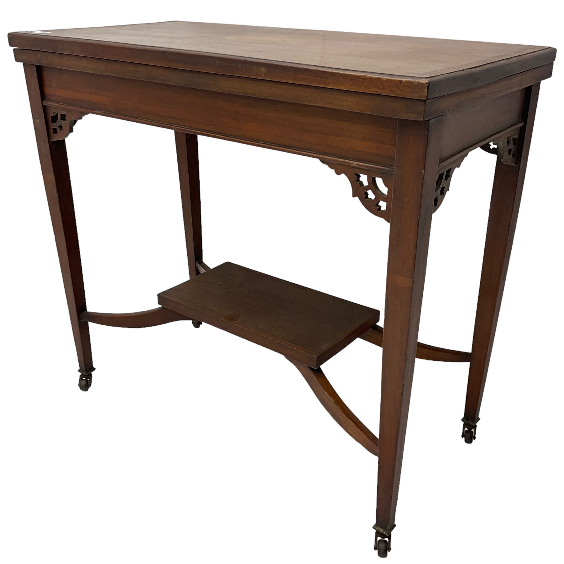 Edwardian inlaid mahogany games table, the rectangular fold-over swivel top decorated with central shell motif inlay and ebony stringing, raised on tapering supports united by shaped X-stretcher and undertier