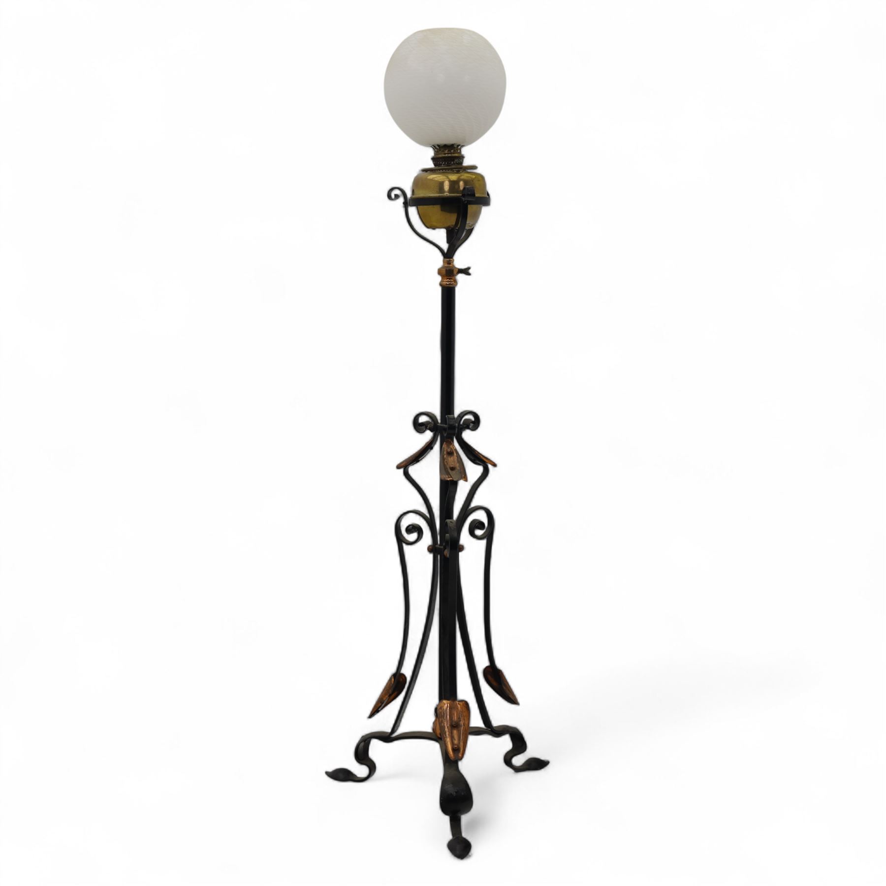 Early 20th-century Art Nouveau style standard lamp, wrought iron scrolled tripod base with copper foliate terminals supporting a brass oil reservoir surmounted by an opaline glass globe shade with spiral patterning, wired for electricity, untested 