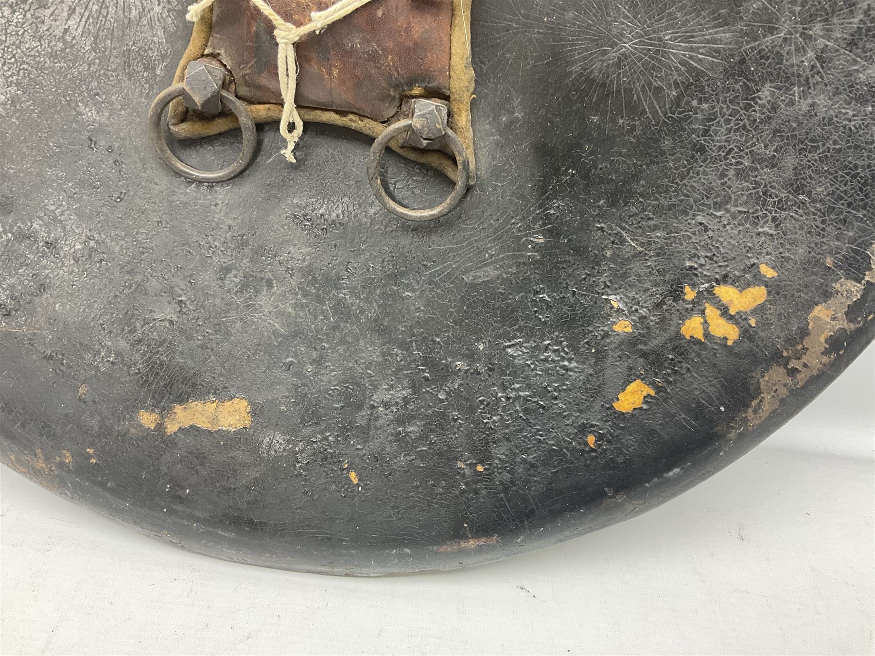 Indian black lacquered hide shield/dhal, of circular convex form with strongly outward-turned brim, fitted at its centre with four metal bosses, each of hemispherical form, with traces of silvered foliate decoration, the bosses corresponding on the inside with four iron rings for enarmes D49cm