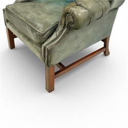 Georgian design mahogany framed wingback armchair, upholstered in rustic pale green buttoned leather with loose seat cushion, raised on square supports united by H-stretcher