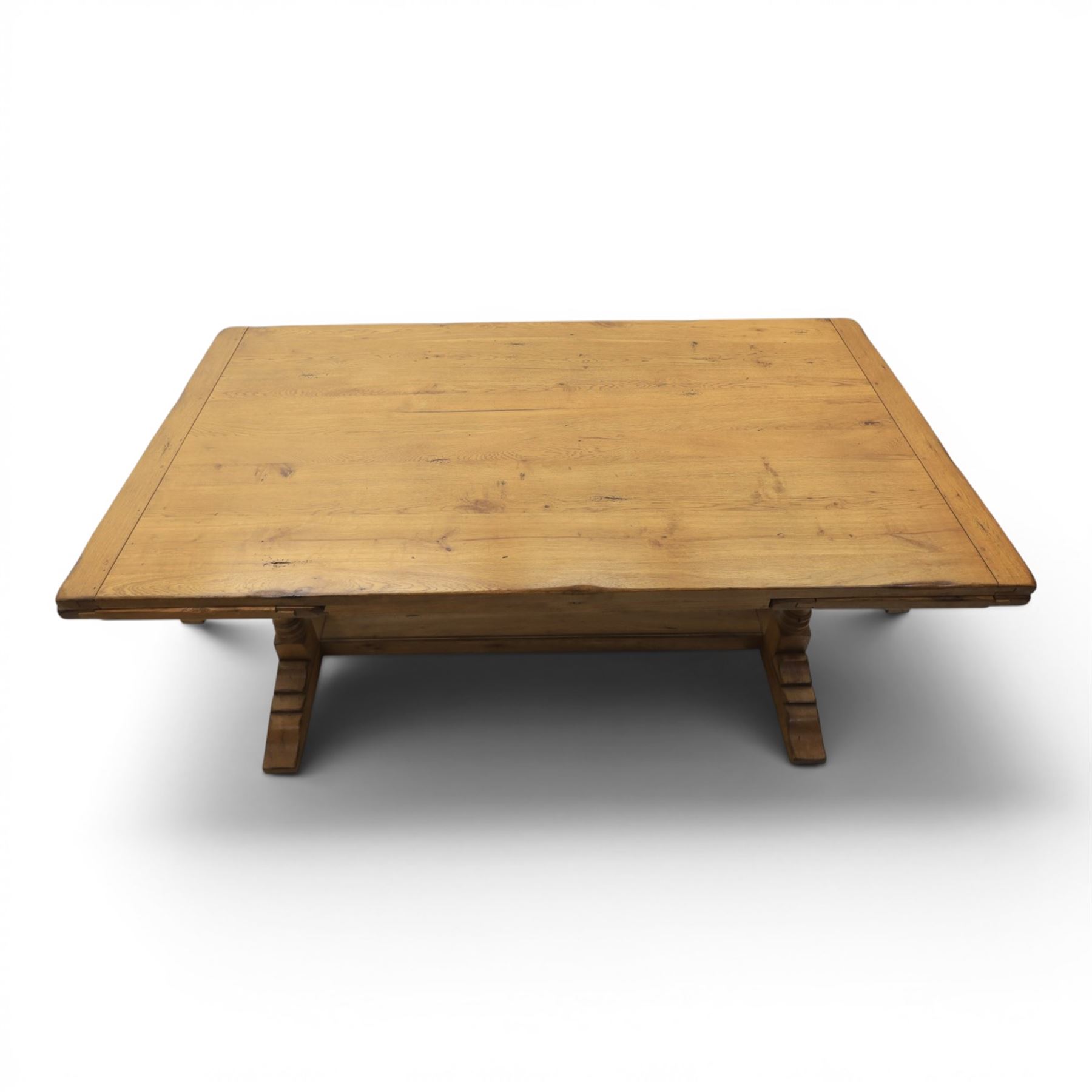 Traditional oak refectory dining table, fitted with draw leaves to either end extending to 257cm, on twin turned and block supports united by a stretcher, terminating in shaped trestle feet
