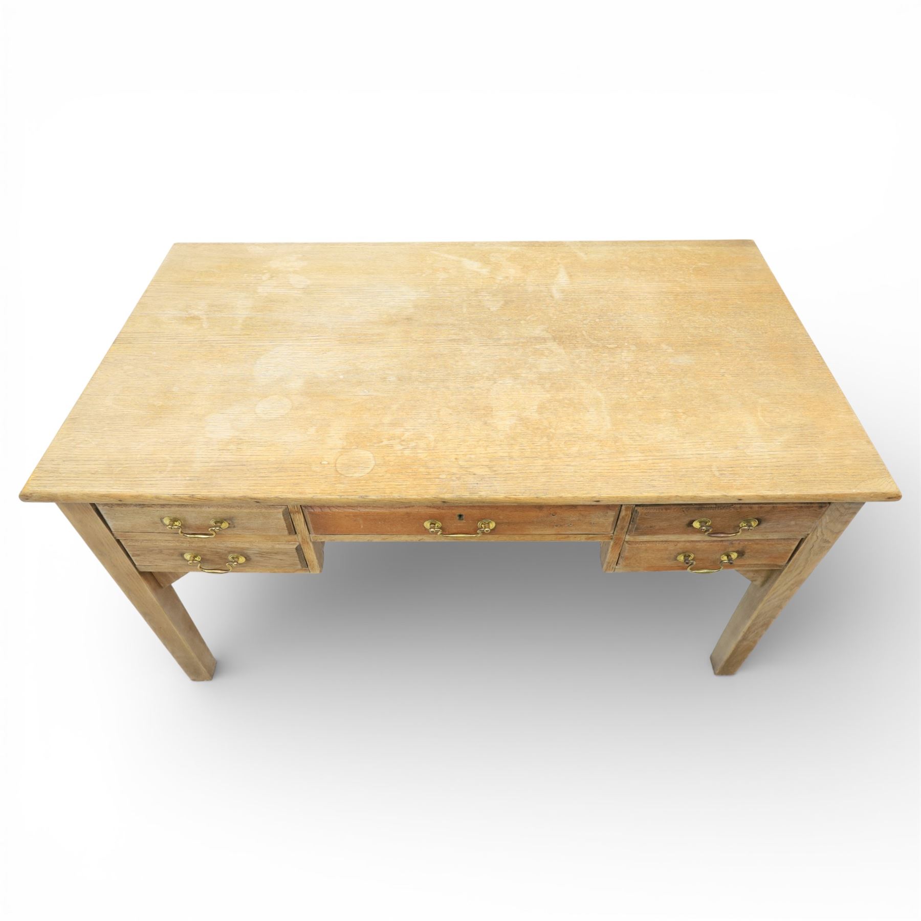 20th century oak kneehole desk, the rectangular top above central drawer and kneehole, flanked by short banks of two drawers, each fitted with brass drop handles, raised upon four plain slightly tapering legs, 75.5cm x 135cm x 73.5cm