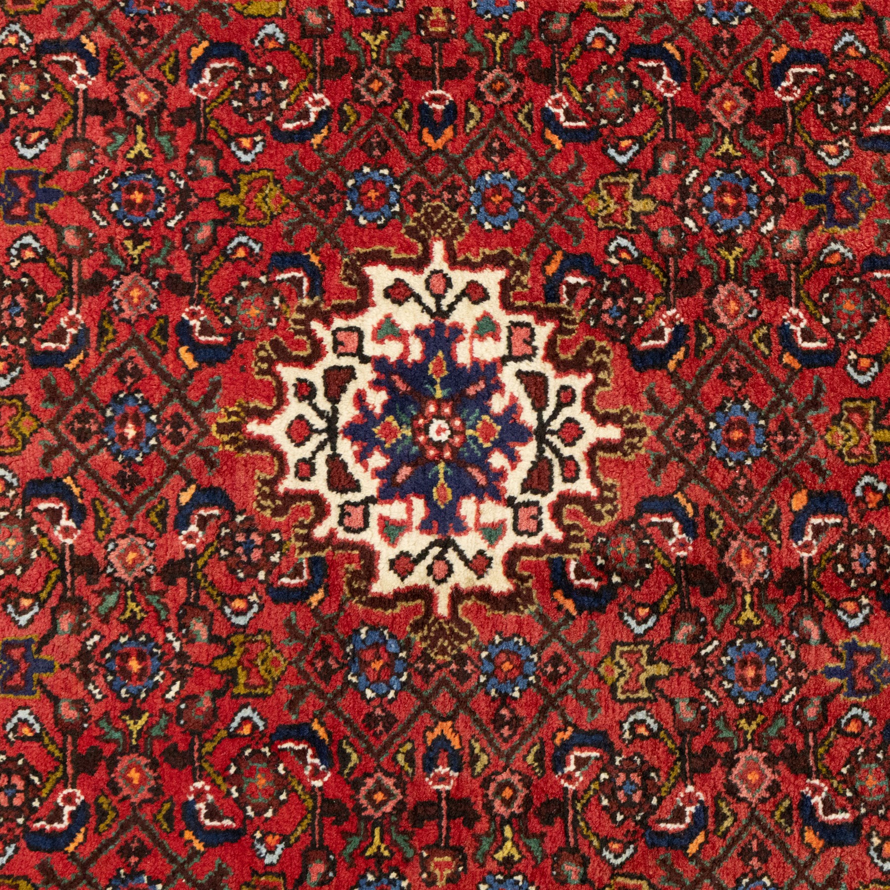 Hamadan hand-knotted rug, red field with small central floral medallion and dense repeating geometric motifs in dark blue, cream and green tones, within multiple patterned borders