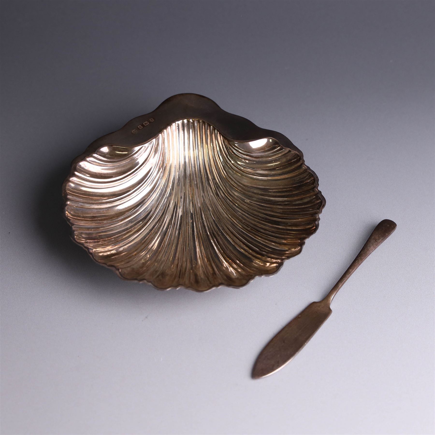 Edwardian silver butterdish in the form of a clam shell and upon four bun feet, hallmarked Williams Birmingham Ltd, Birmingham 1905, with a silver plated butter knife, contained within a fitted tooled leather case, width of dish 13cm