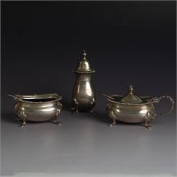 Mid 20th century silver three piece cruet set, comprising pepper shaker, open salt, mustard pot with cover and two condiment spoons, all of oval form with oblique gadrooned rims and upon four paw feet, hallmarked Adie Brothers Ltd, Birmingham 1957, with blue glass liners