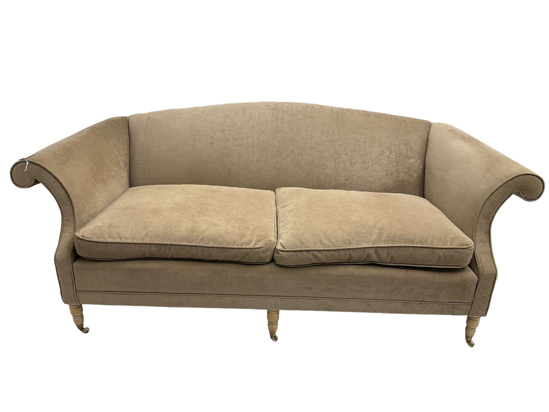 Traditional three seat sofa, curved back over scrolled arms, upholstered in crushed beige fabric with matching loose cushions, on turned front supports with brass and ceramic castors, together with matching footstool