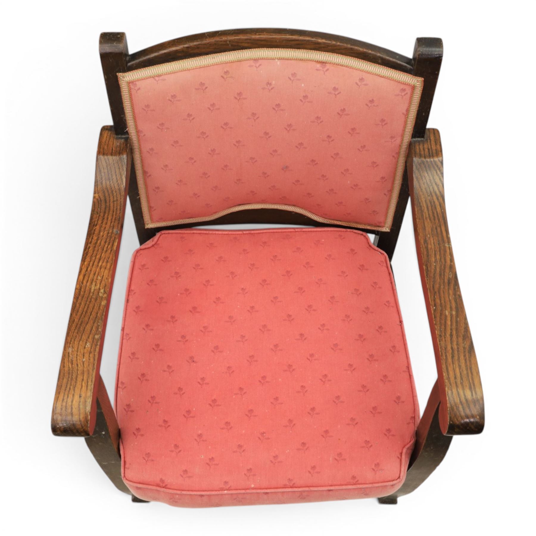 Early 20th century small oak open armchair, arched upholstered back with brass stud border over shaped seat cushion upholstered in pink foliate fabric, shaped open arms on square supports