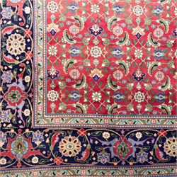 North West Persian Tabriz hand-knotted carpet, herati-type field in deep red with an all-over field densely decorated with scrolling floral sprays and palmettes on a lattice ground enclosed by a dark blue main border filled with stylized floral motifs and interlacing tendrils flanked by multiple guard stripes, with cotton fringe ends 