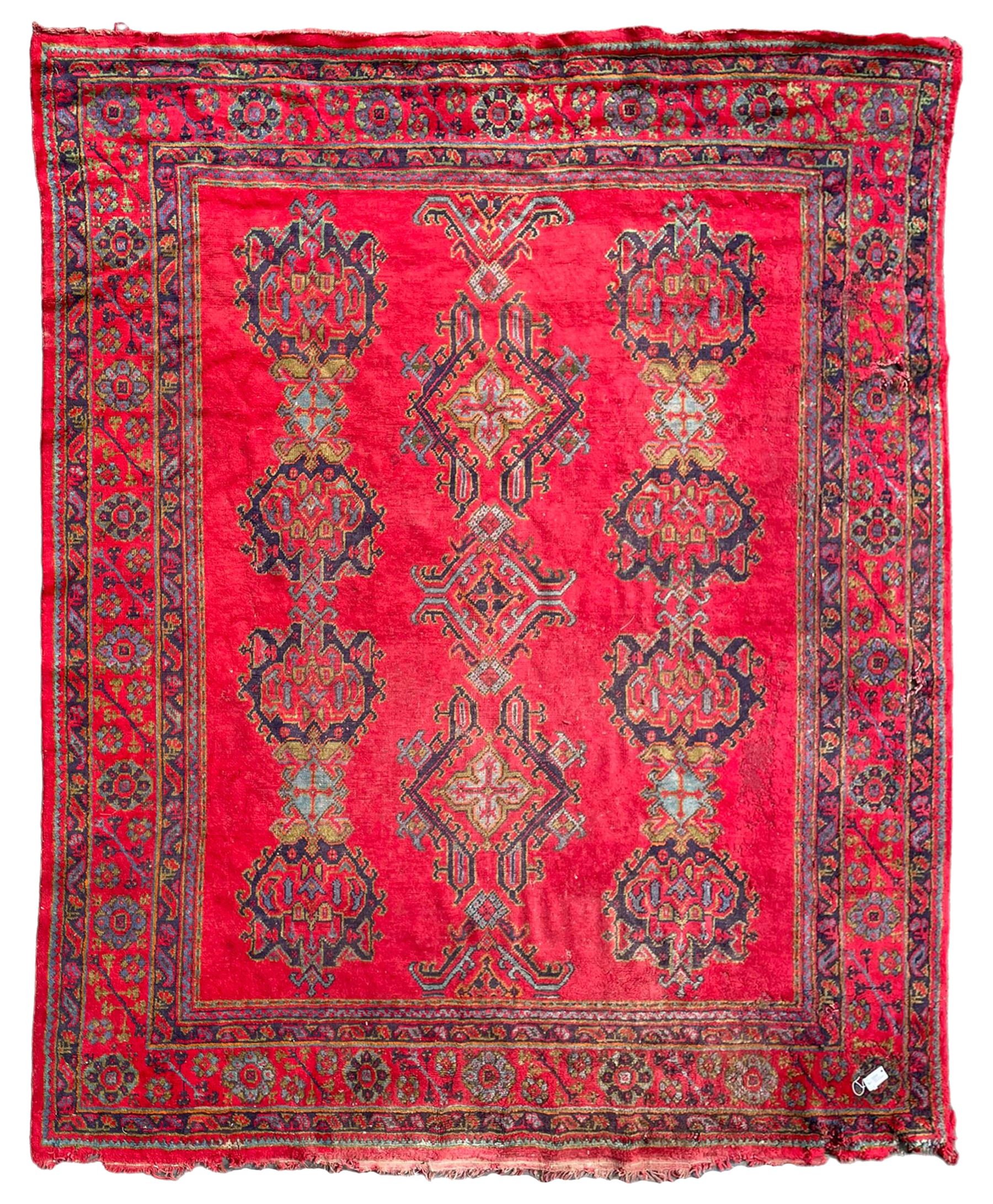Early 20th century Western Anatolia Turkish Oushak crimson ground carpet, the field decorated with rows of Herati and Palmette medallions, the main border decorated with stylised flower head motifs within guard stripes