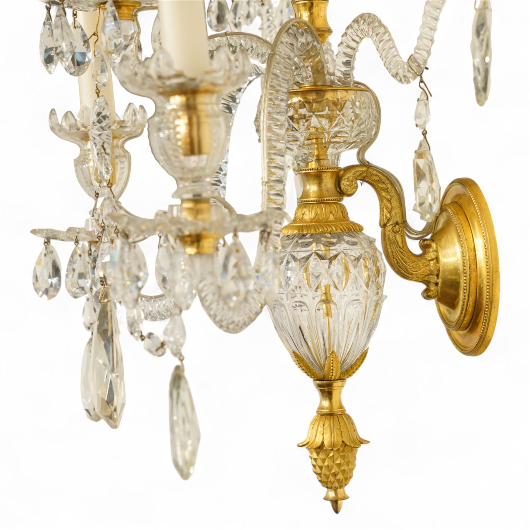 Pair of George III ormolu and cut-glass wall-lights, each with a tall central urn-shaped finial above a series of faceted glass spires and scrolled branches, the ormolu-mounted nozzles and drip pans hung with festoons of cut-glass drops and pear-shaped pendants, the lower section centred by a pineapple finial, wired for electricity