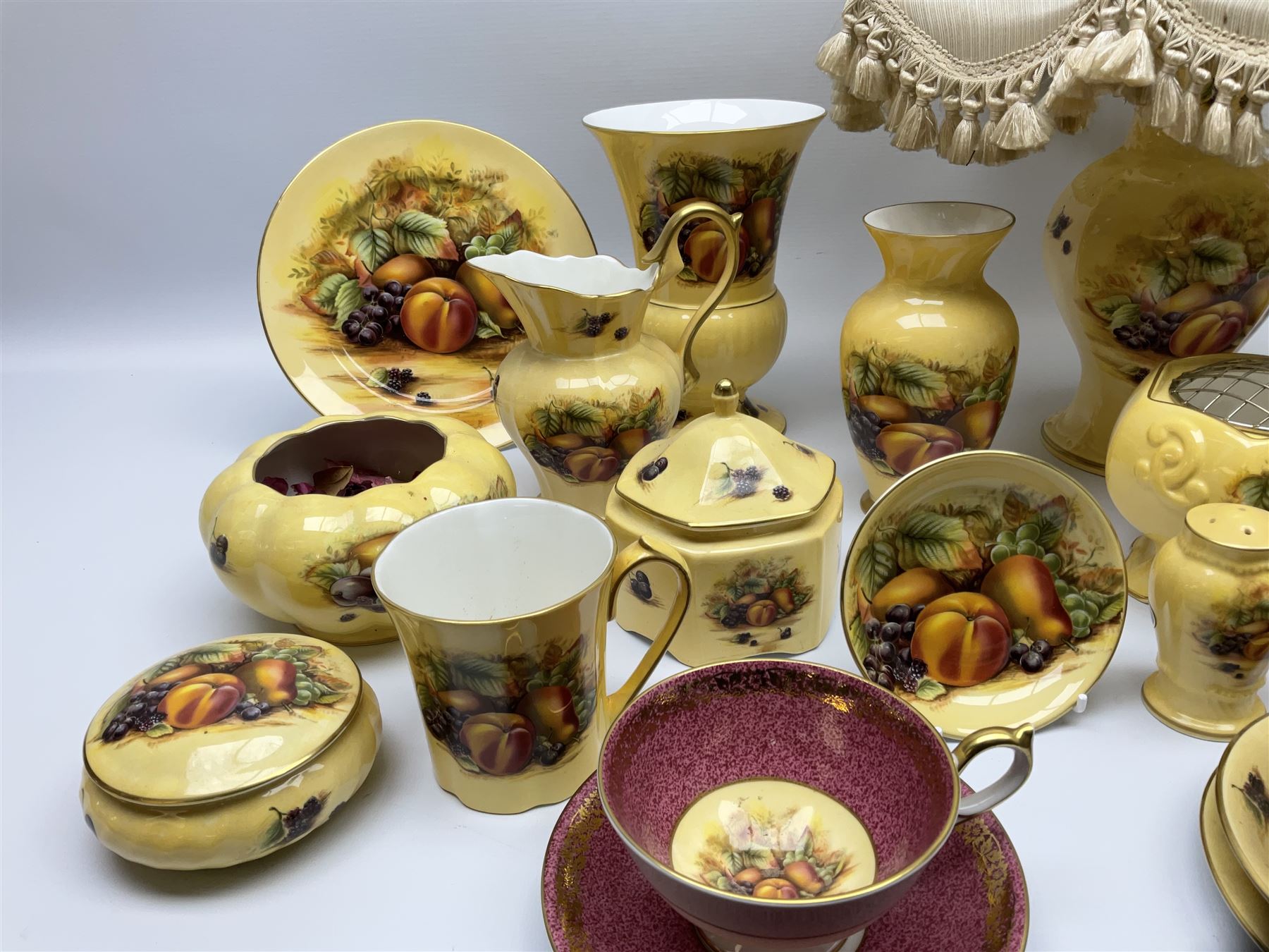 Collection of Aynsley Orchard Gold pattern wares, comprising lamp base, three jars and covers, six vases or various size and form, large jug, lidded dish, pair of cruets, pair of candlesticks, mug, two pin dishes, lobed dish, tea cup, saucer, size plate, and cake plate, and two further cups and saucers, each cup decorated with central Orchard Gold reserve to the interior against a mottled pink or green ground. 