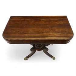 Regency rosewood fold over card table, the rectangular top with rounded corners and gadrooned edge opening to reveal a green baize lined interior, raised upon convex lobbed and acanthus pedestal and four fluted sabre legs, terminating in brass lion paw feet and castors