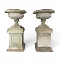Pair of weathered cast stone Neoclassical design garden Kylix shape urns, foliate moulded rim over a gadrooned underbelly, the scalloped socle over a rectangular pedestal with faux-panelled sides, stamped with stylised ‘H’ monogram
