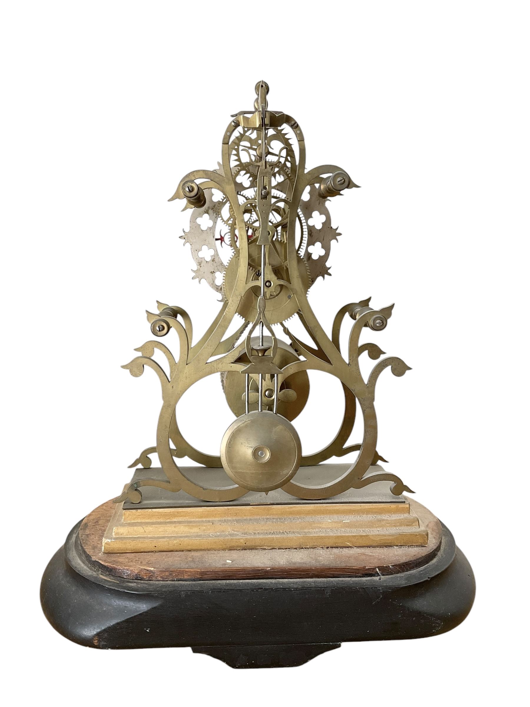 English-Late 19th century 8-day Skeleton clock on an oval ebonised base c1880, with pierced brass plates and silvered chapter ring, Roman numerals and gothic trefoil hands, chain driven five-pillar fusee movement and pierced mainspring barrel cap, timepiece movement with key and pendulum. 