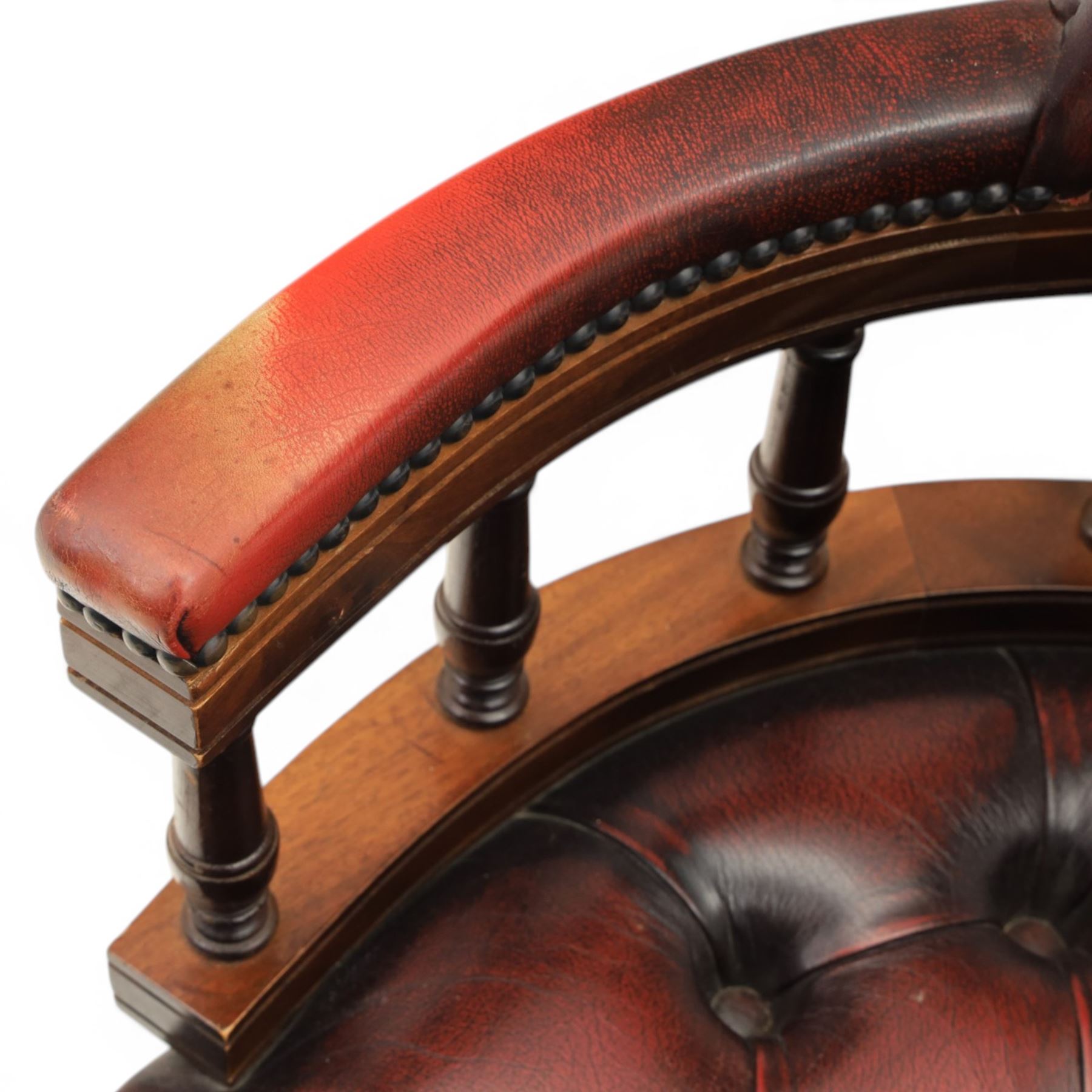 Captains swivel desk chair upholstered in oxblood leather, buttoned back and seat, shaped arm bow raised on turned spindles, five spoke base raised on castors