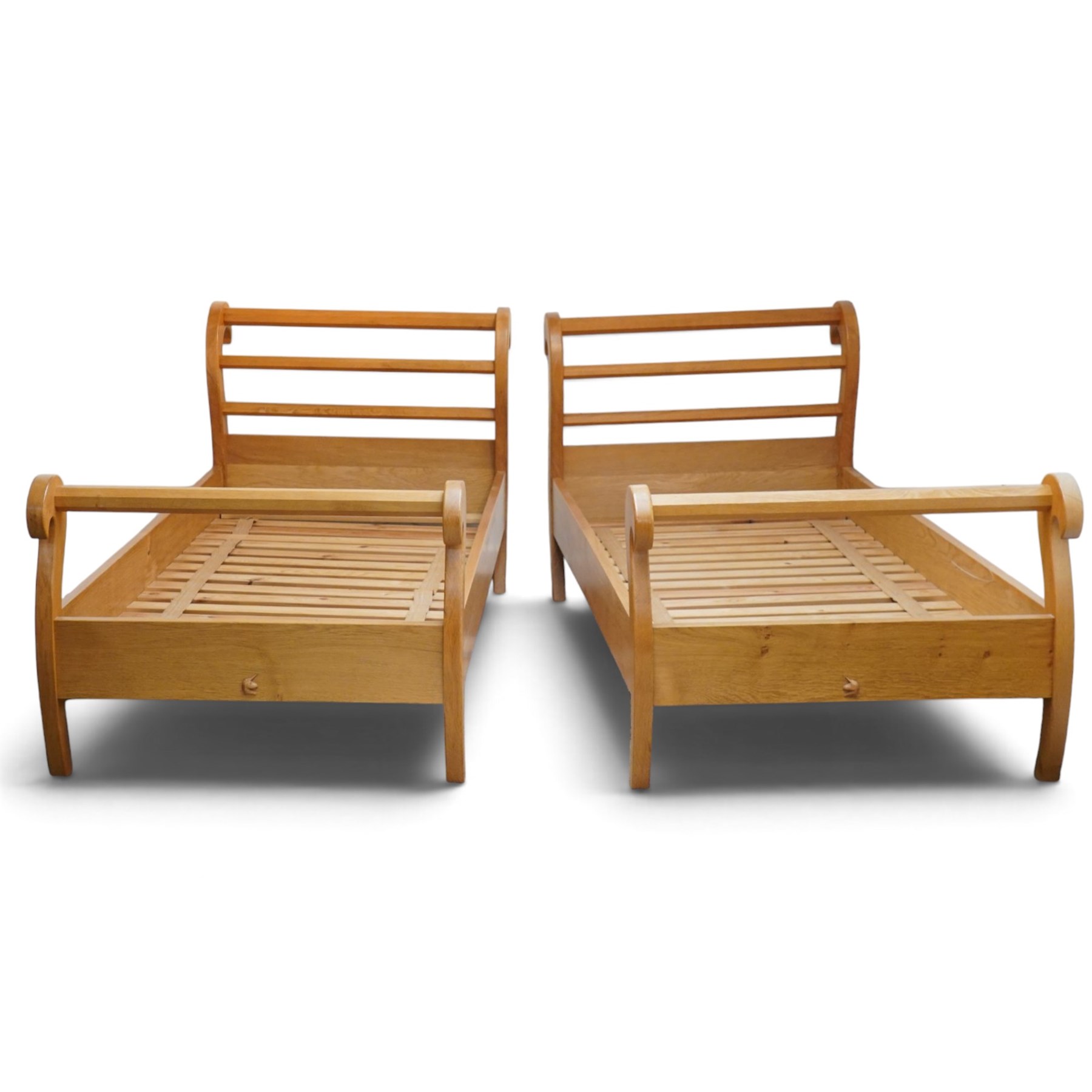 Unicornman - pair of craftsman-made oak single beds, of sleigh shape with scrolled head and foot-boards with octagonal stretchers, slatted base, raised on inward-splayed squared supports, applied with carved unicorn signature, by Geoff Gell of Coxwold