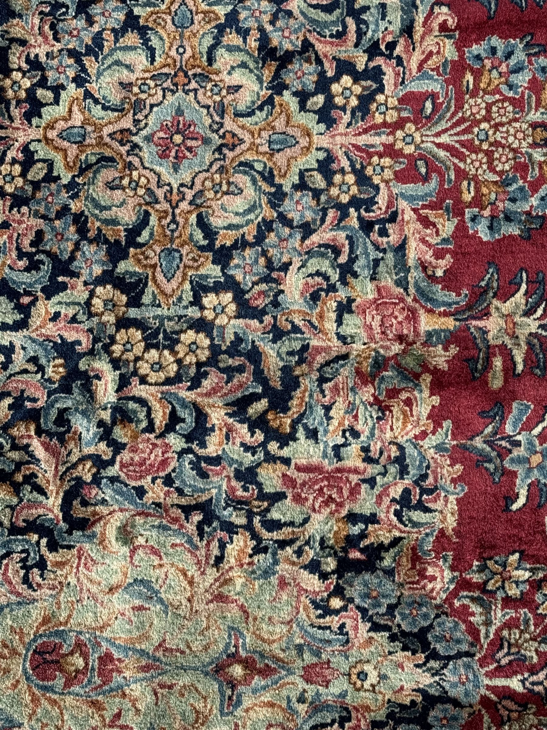 Persian Kirman carpet, the bold ruby field hosting a multi-lobed central medallion, embellished with scrolling vines and floral sprays, edged by layered borders and trimmed with short fringe