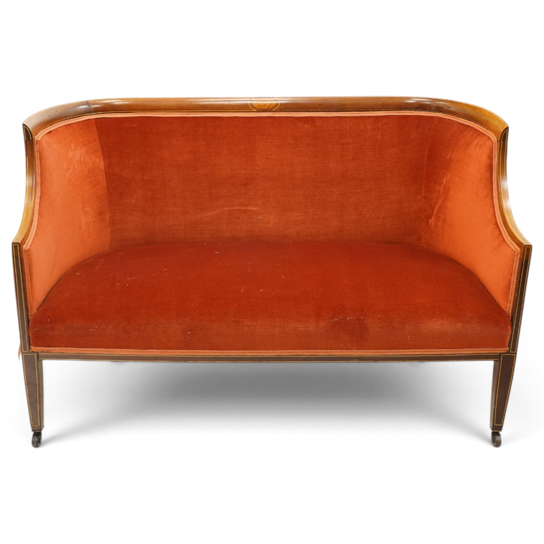 Edwardian inlaid mahogany tub two seater settee, traditional shape with satinwood stringing, upholstered in crimson fabric with sprung seat, on square tapering supports with castors