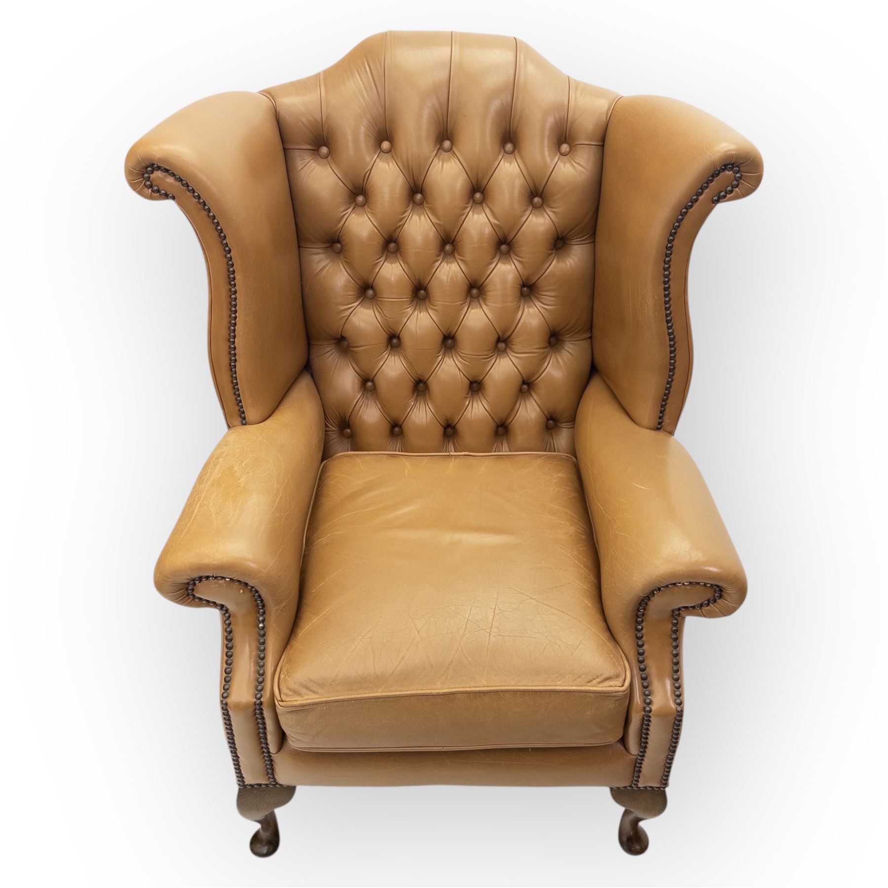 Contemporary set of two tan leather armchairs, comprising a deep-buttoned chesterfield and a matching wingback chair, both with rolled arms, studded borders