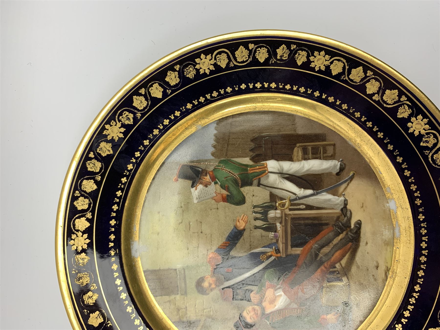 19th century Rihouet Paris porcelain cabinet plate, decorated with a central panel illustrating three French soldiers around a bottle laden table, one surveying a note, within a dark blue gilt detailed border, with French inscription verso, and red printed mark Rihouet Rue de la Paix A Paris and green fish mark, possibly for Perche, D23cm 



