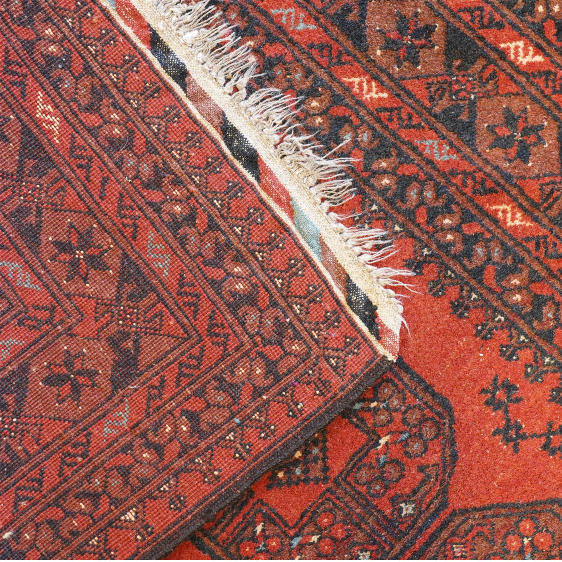 Bokhara red ground rug, the field decorated with three Gul motifs, within multiple borders with repeating geometric patterns (146cm x 103cm); together with an Afghan rug (144cm x 100cm)