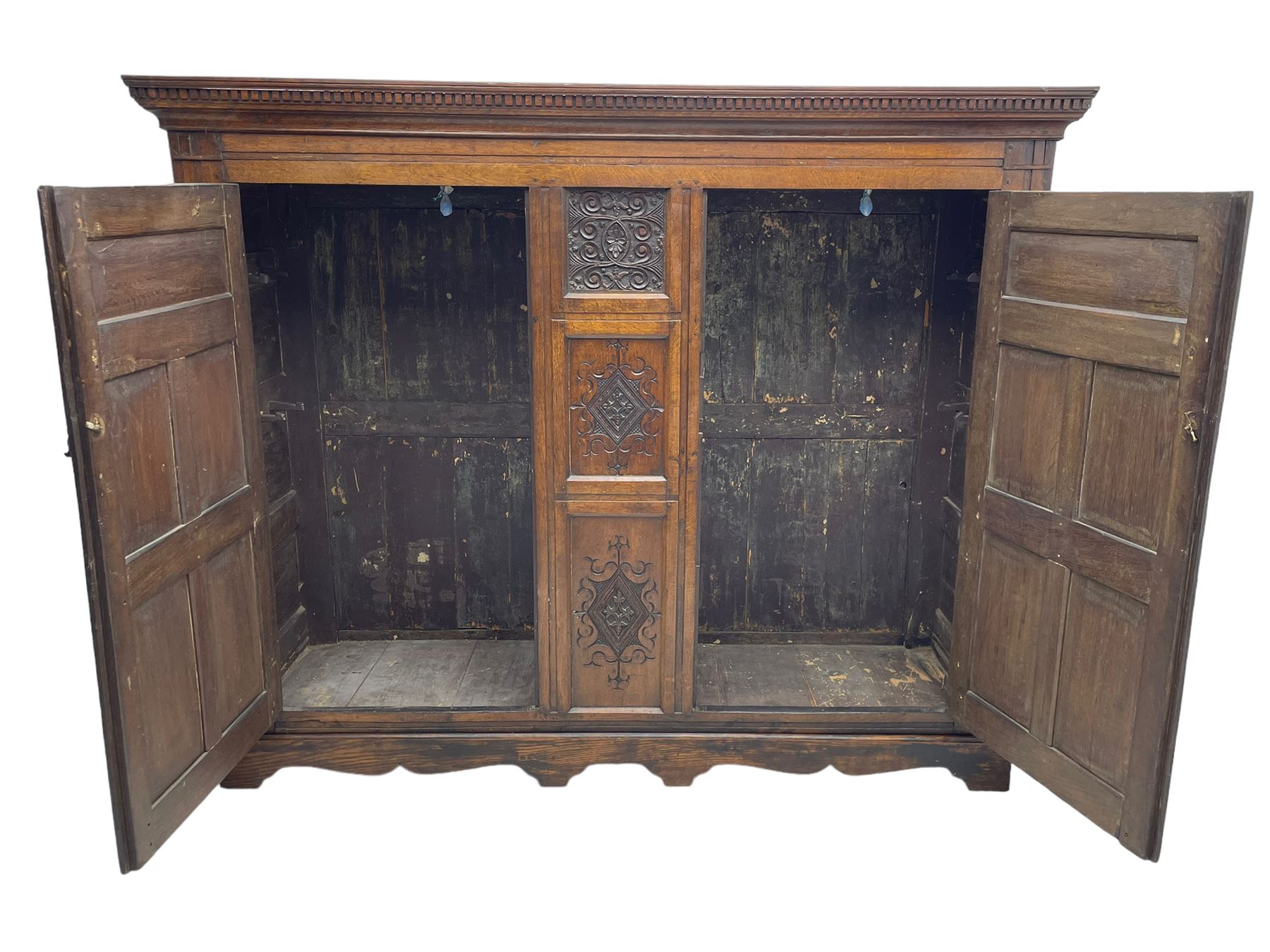 Large 18th century and later oak livery cupboard, projecting moulded and dentil cornice, sunken fillet moulded frame, triple vertical panelled central upright, enclosed by two doors each with five panels, the top row of panels carved with stylised scrolls, the lower panels carved with foliate lozenges, on shaped bracketed skirt base 