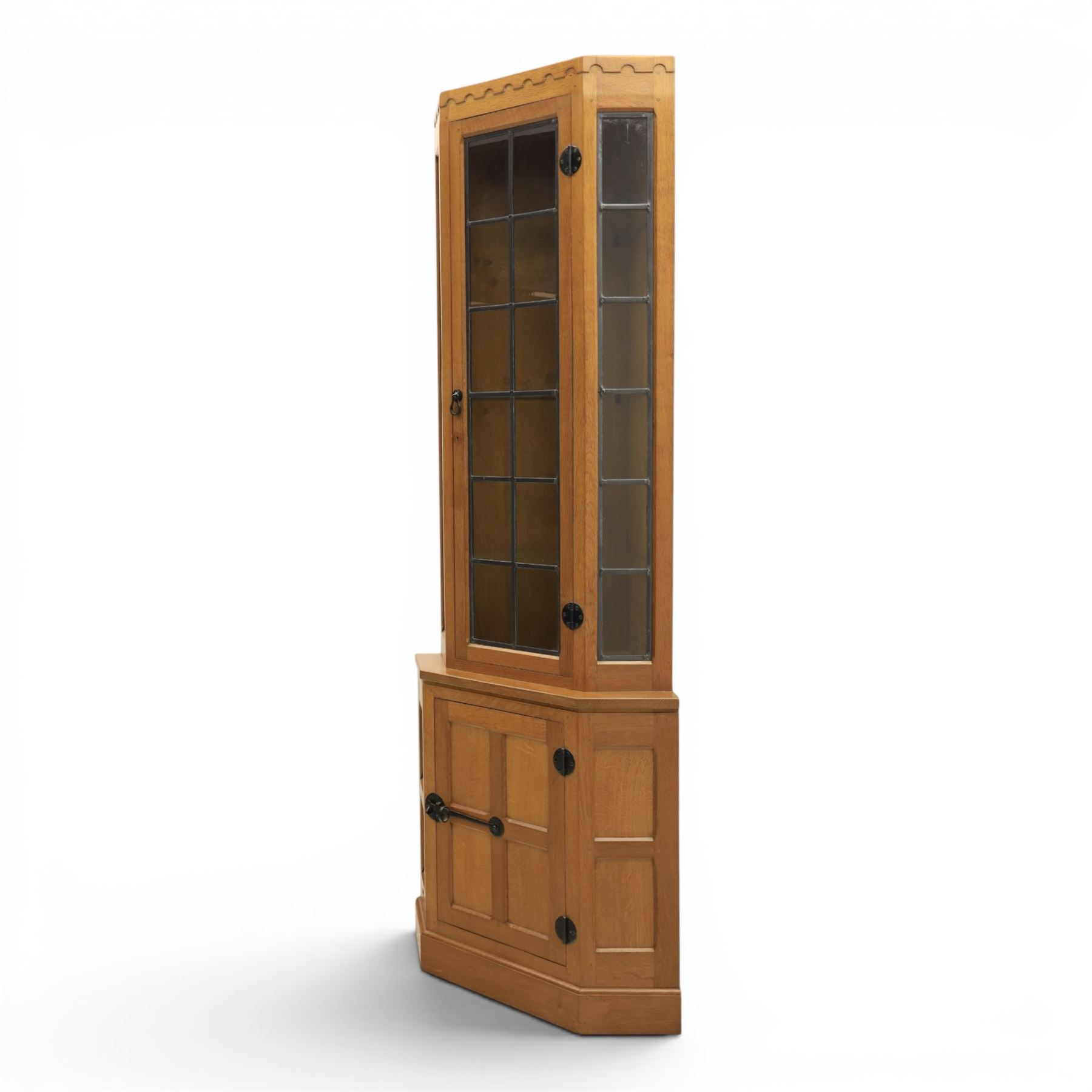 Mouseman - oak floor standing corner cabinet, scalloped cornice above a leaded glass cabinet, blackened metal hinges and latches, with carved mouse by the workshop of Robert Thompson of Kilburn