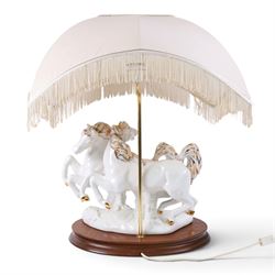Italian-style ceramic table-lamp featuring two white running horses with gold accents, with cream tasselled lampshade, upon a wooden base, approx. H60cm W40cm