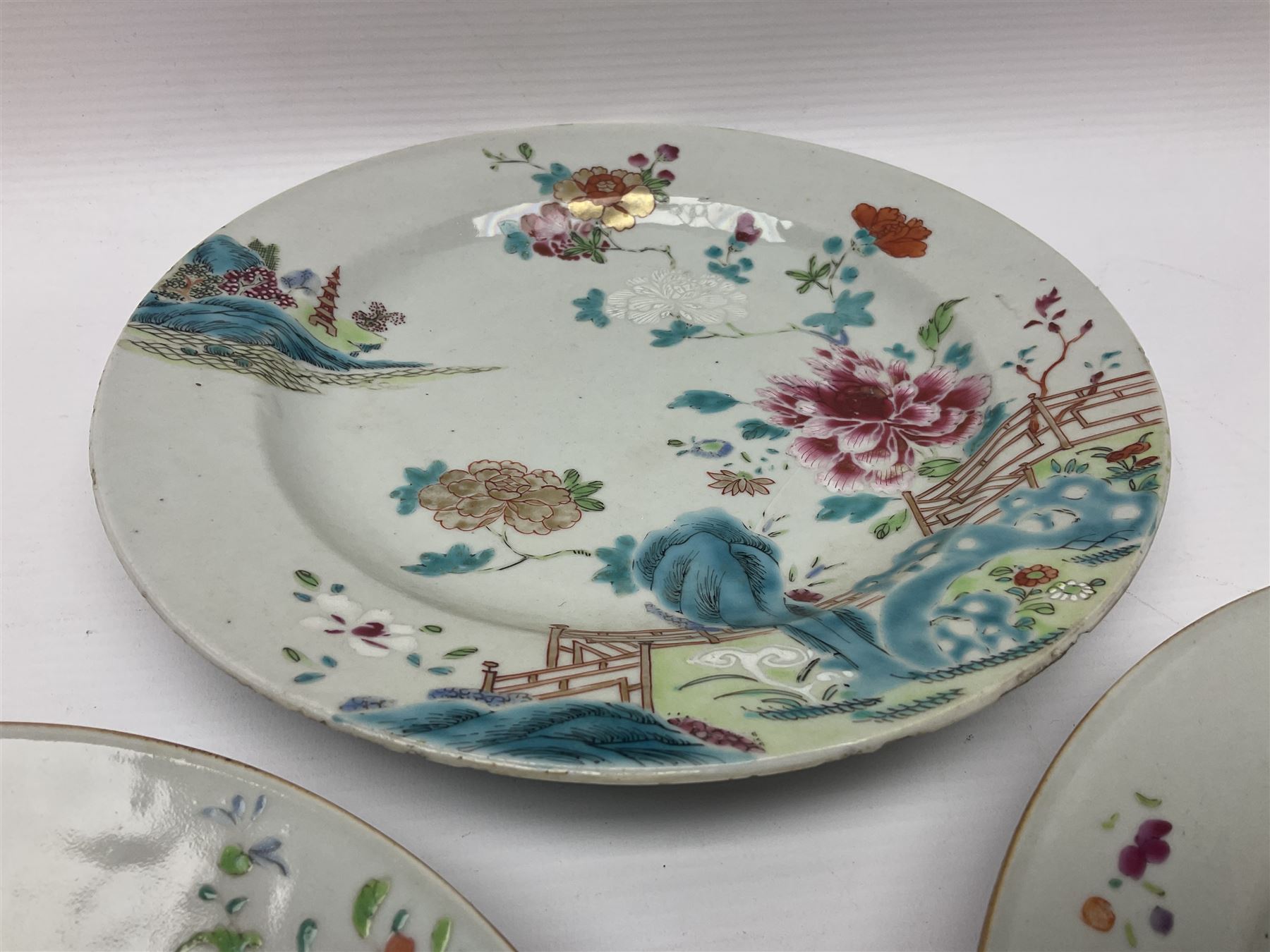 Three 18th century Chinese Famille Rose plates, the first example enamelled with blossoming peonies, rockwork and fence, the other two examples of similar design, decorated with blossoming peonies and sprigs within shaped inner borders, each approximately D23cm
