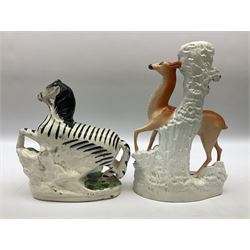 Group of 19th century Staffordshire figures, to include spill vase modelled with doe raising one fore leg above fawn against tree stump, flatback Zebra figure with front leg raised, figure of a recumbent sheep on a mound base before pink flowering bocage, pair of later seated cats on cushions etc, tallest example H29cm