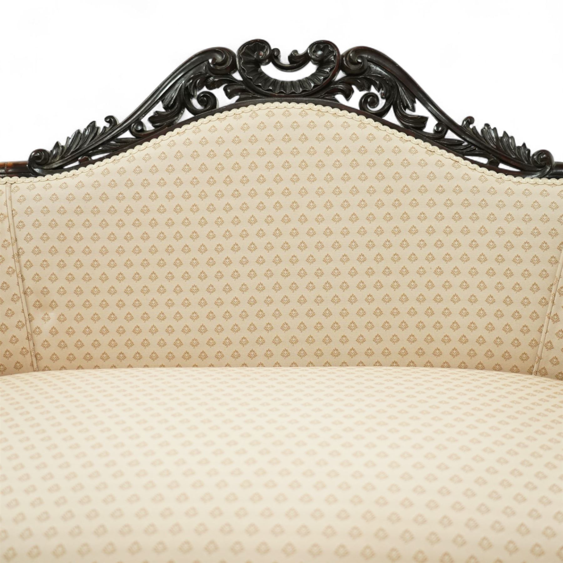 Victorian mahogany upholstered settee, the shaped back with pierced foliate carved cresting, upholstered in cream patterned fabric with serpentine seat, on cabriole front legs with brass castors