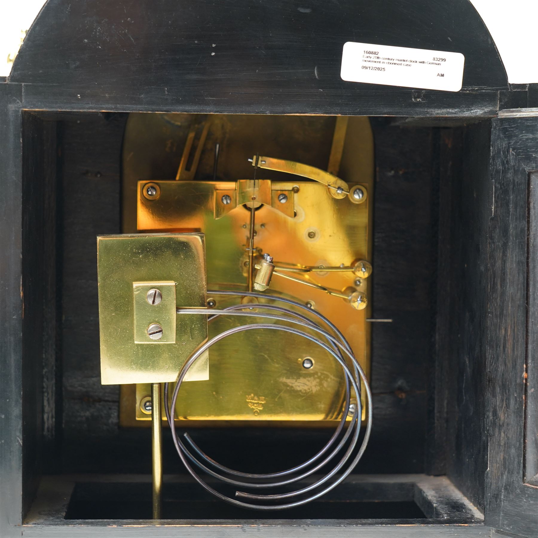 Winterhalder & Hoffmeier-8-day early 20th century mantel clock with an ebonised finish, break arch pediment and two matching brass finials, conforming glazed door with a cast brass bezel flanked by reeded quarter pilasters, on a moulded plinth with scroll feet, brass dial with cast spandrels and strike/silent and pendulum regulation dials to the arch, matted dial centre with a silvered chapter, Roman numerals  and gothic steel hands, dial pinned to a quarter striking movement sounding the quarters on two gongs and hours on one. With Pendulum.
