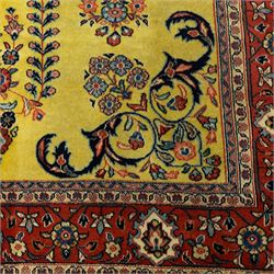 Persian Sarough hand-knotted carpet, golden yellow ground, with an all-over floral design centred by a small floral motif, the field decorated with mirrored flowering sprays, scrolling vines and dark navy foliate corner motifs, enclosed by a terracotta border with repeating flowerheads and palmettes, flanked by narrow guard stripes, with cotton fringes