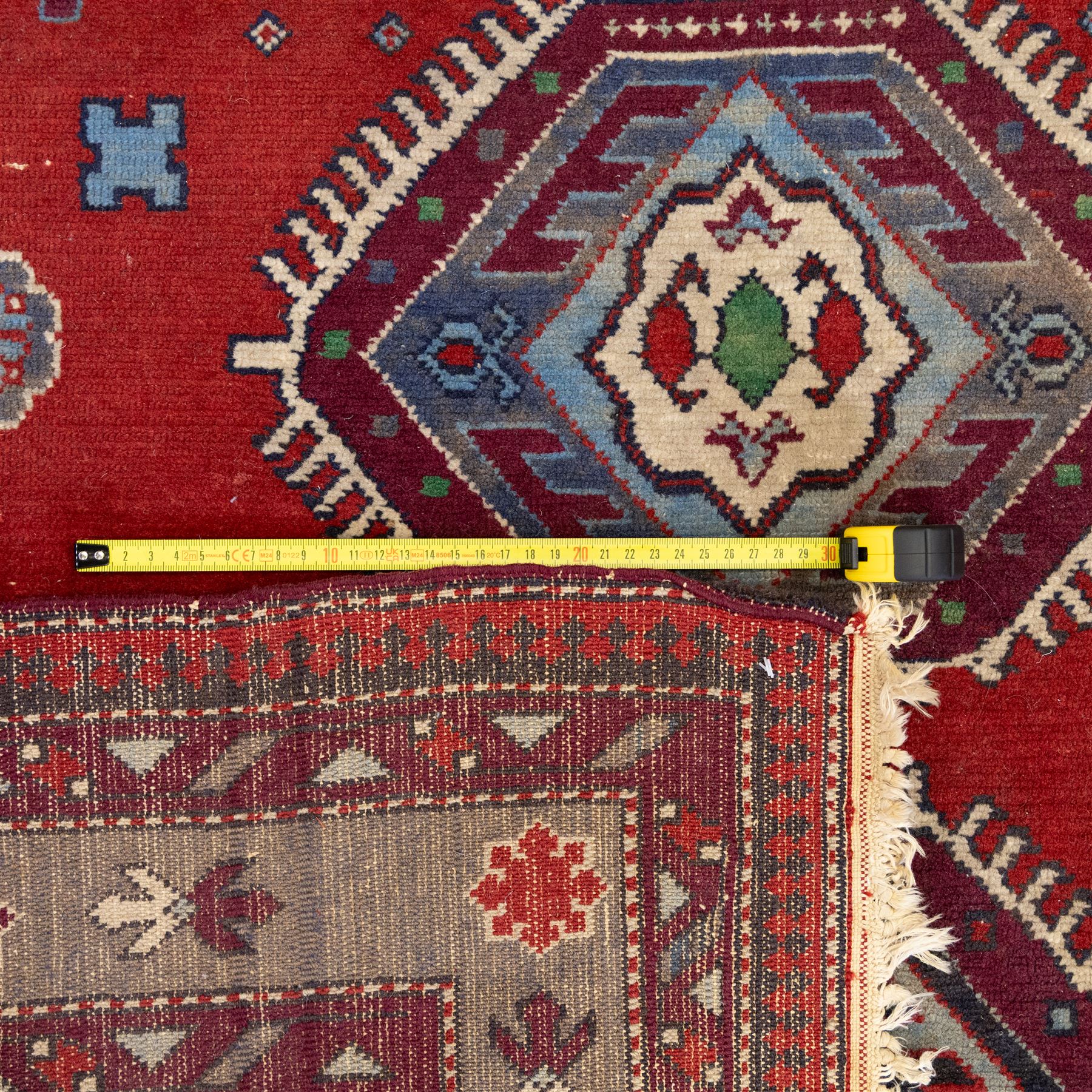 Caucasian Kazak rug, red field decorated with a column of stepped hexagonal medallions in blue, ivory, and crimson, flanked by stylized floral and geometric motifs, enclosed by multiple borders of rosettes and hooked designs 