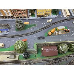 Table top 'N' gauge continental scenic layout as a split level town with various loops of track, station with numerous platforms, engine shed, assorted buildings, roads with motor vehicles and figures, tunnels, trees, river with bridge, tram depot etc 122 x 52cm