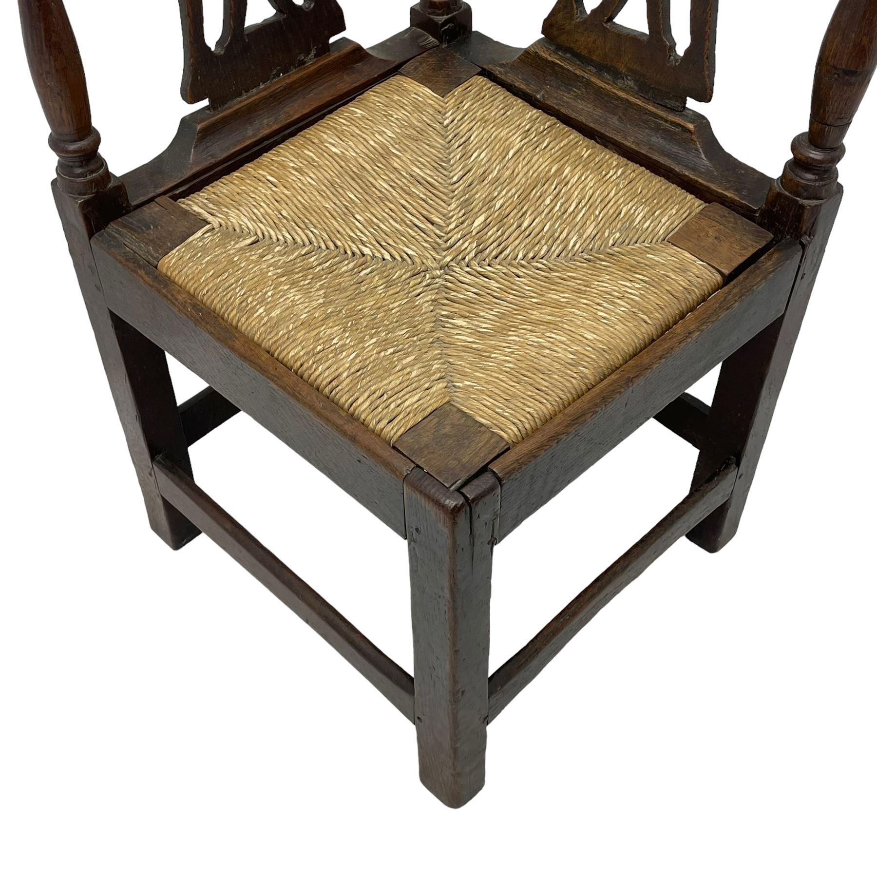18th century country elm and oak corner chair, the shaped cresting rail terminating to swept arm resets, supported by turned columns and pierced shaped splats, over a drop-in rush seat, raised on square supports united by box stretcher