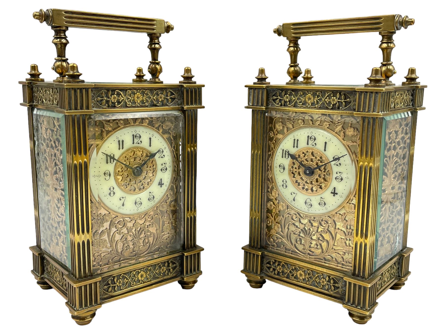 French - Matching pair of Edwardian 8-day timepiece carriage clocks with bevelled rectangular glass panels and overlaid friezes in gilt repousse work with fretted dial masks,  circular enamel chapter ring with Arabic numerals and steel spade hands, both clocks with single train movements, one movement with a jewelled cylinder platform escapement and the other with a jewelled and silvered lever platform escapement.
No Keys.